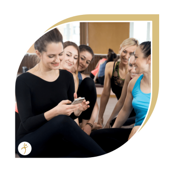 6 junge Frauen in Fitnesskleidung sitzen dicht beieinander und schauen auf ein Handy